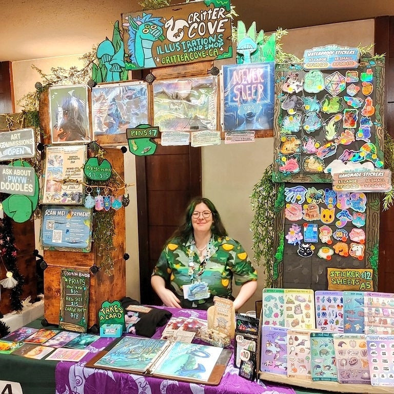 Person standing behind a table with various items and signs at a booth titled 'Critter Cove'.